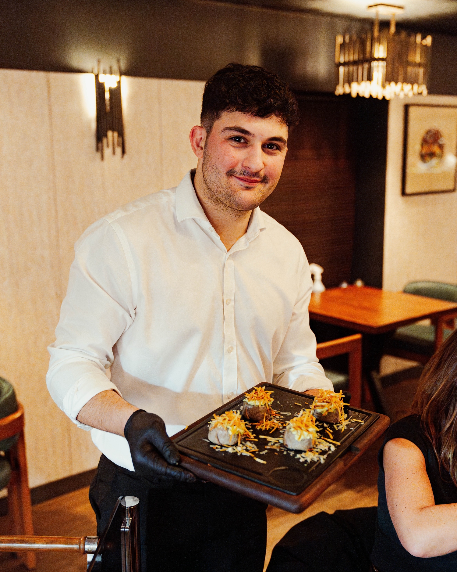 Waiter presenting a board of loaded potatoes