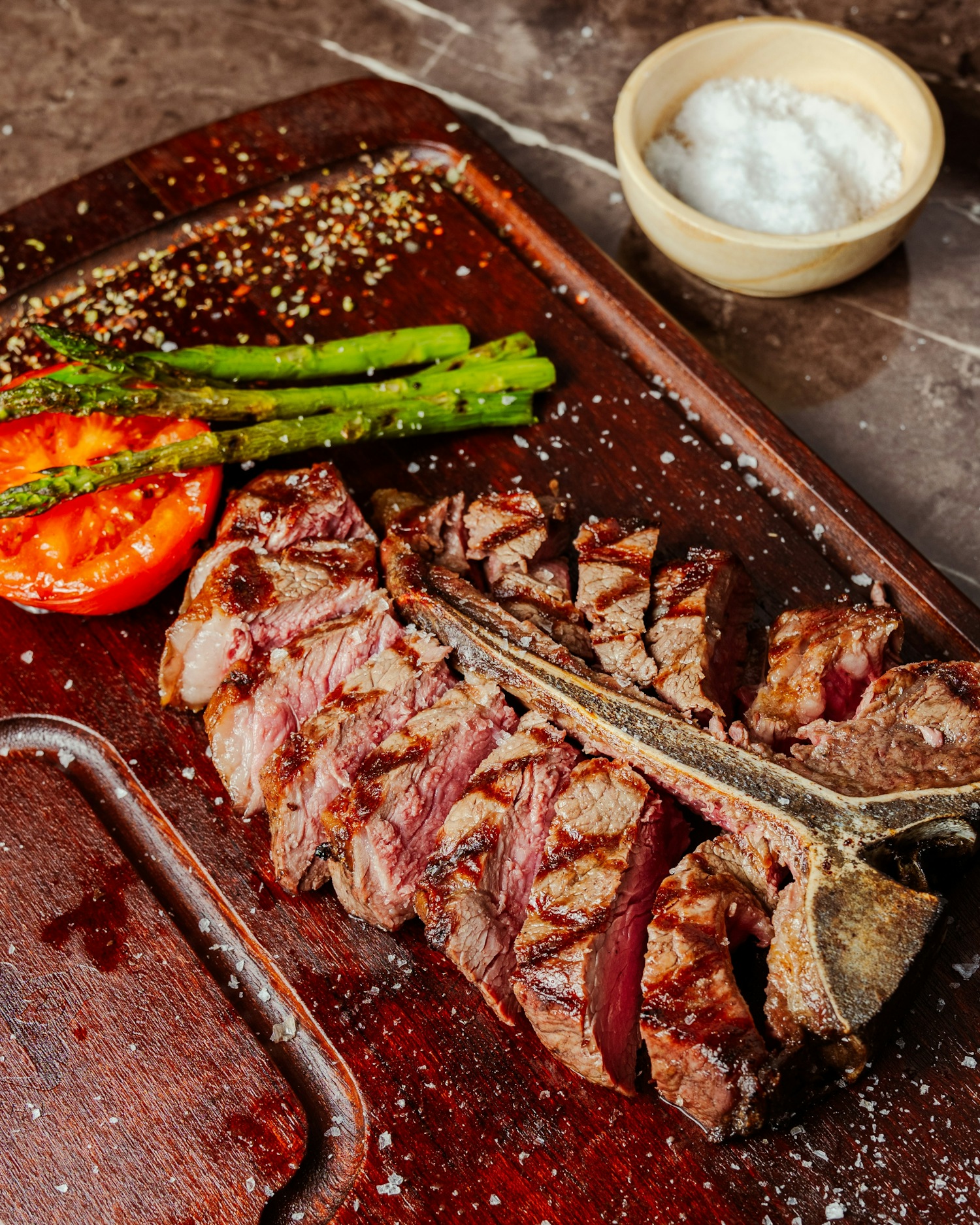 Sliced T-bone steak on a board with asparagus and salt