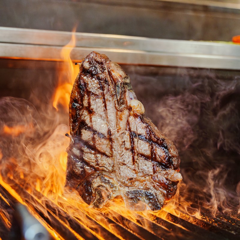 A steak searing over the bespoke charcoal grill